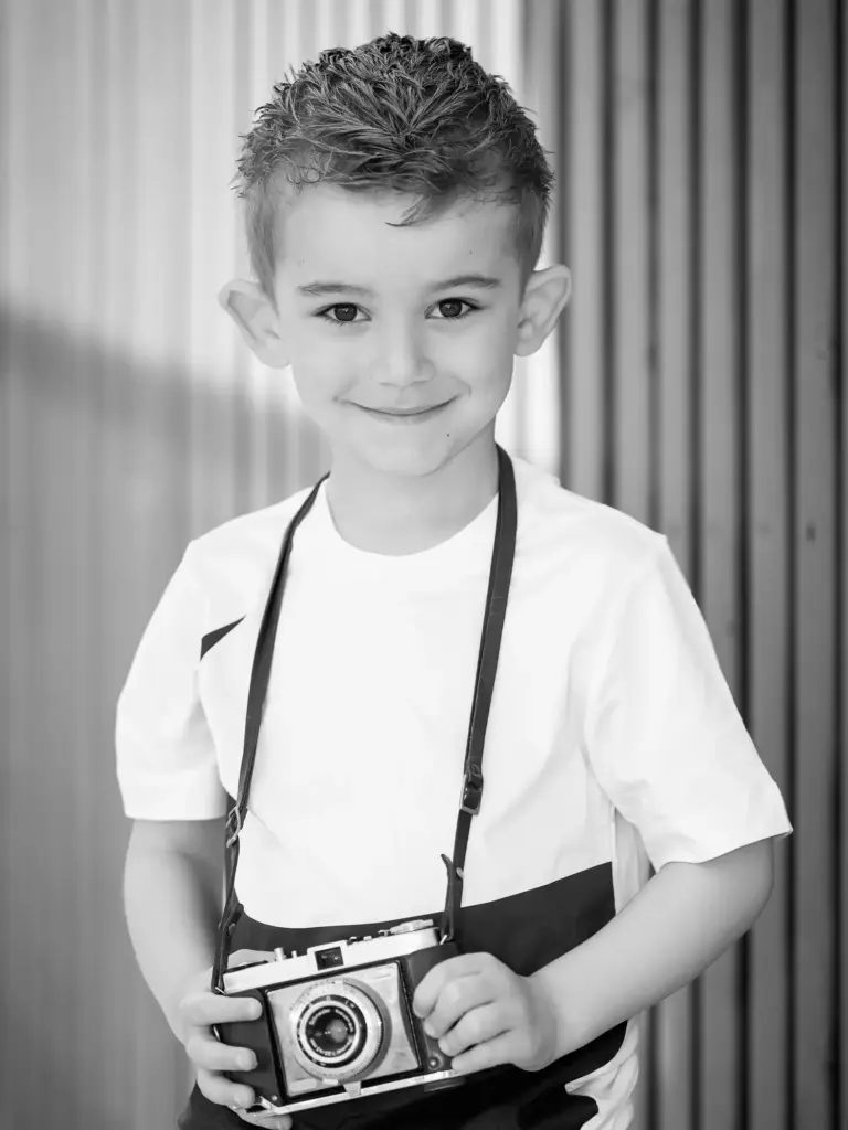 Schwarzweiß-Porträt eines Jungen mit alter Fotokamera